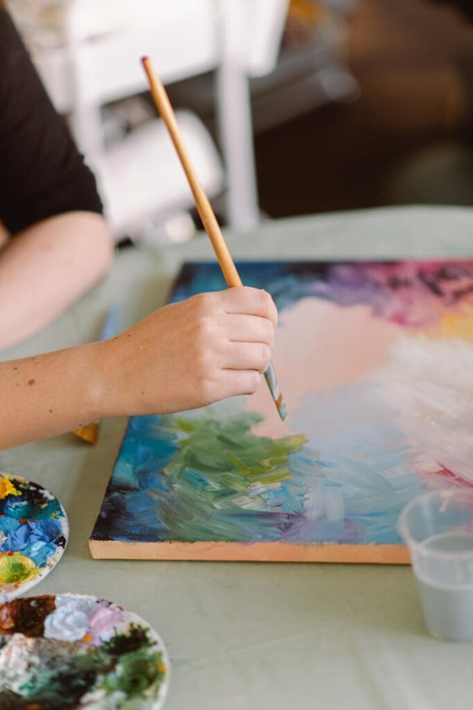 An artist painting with colorful strokes in a sunlit home studio.