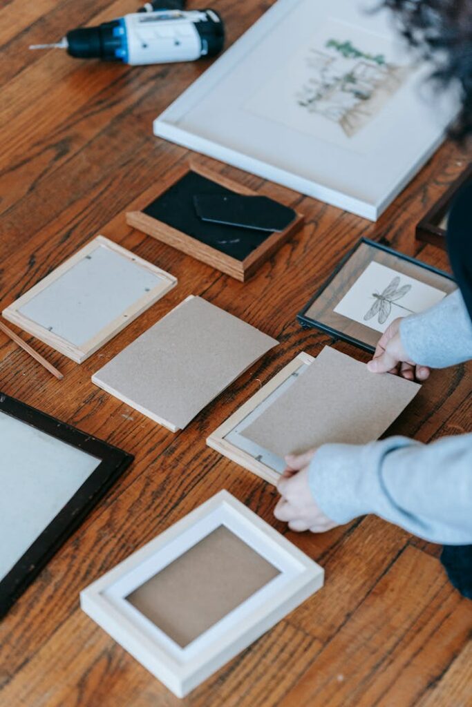 Person arranging picture frames on a wooden floor, preparing for home decoration.