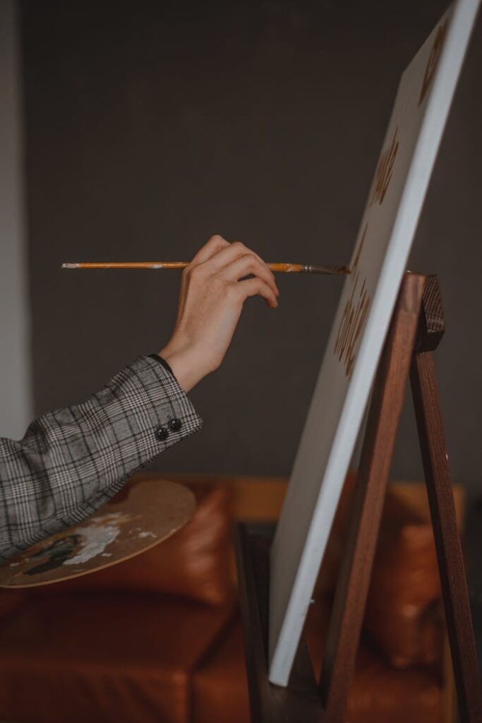 Close-up of an artist's hand painting on canvas using a paintbrush indoors.